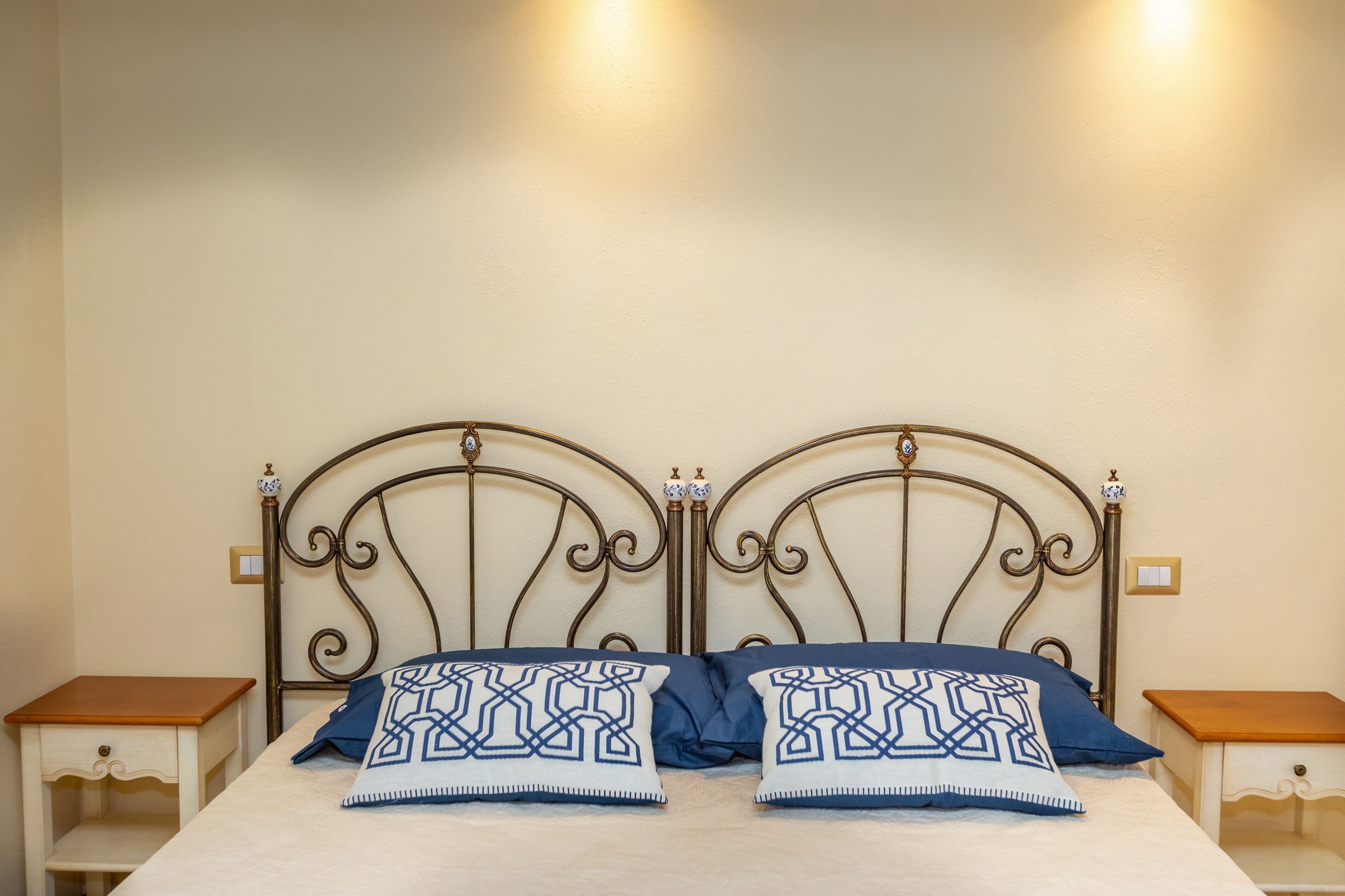 A double bed with a metal headboard, two bedside tables, and decorative wall sconces.