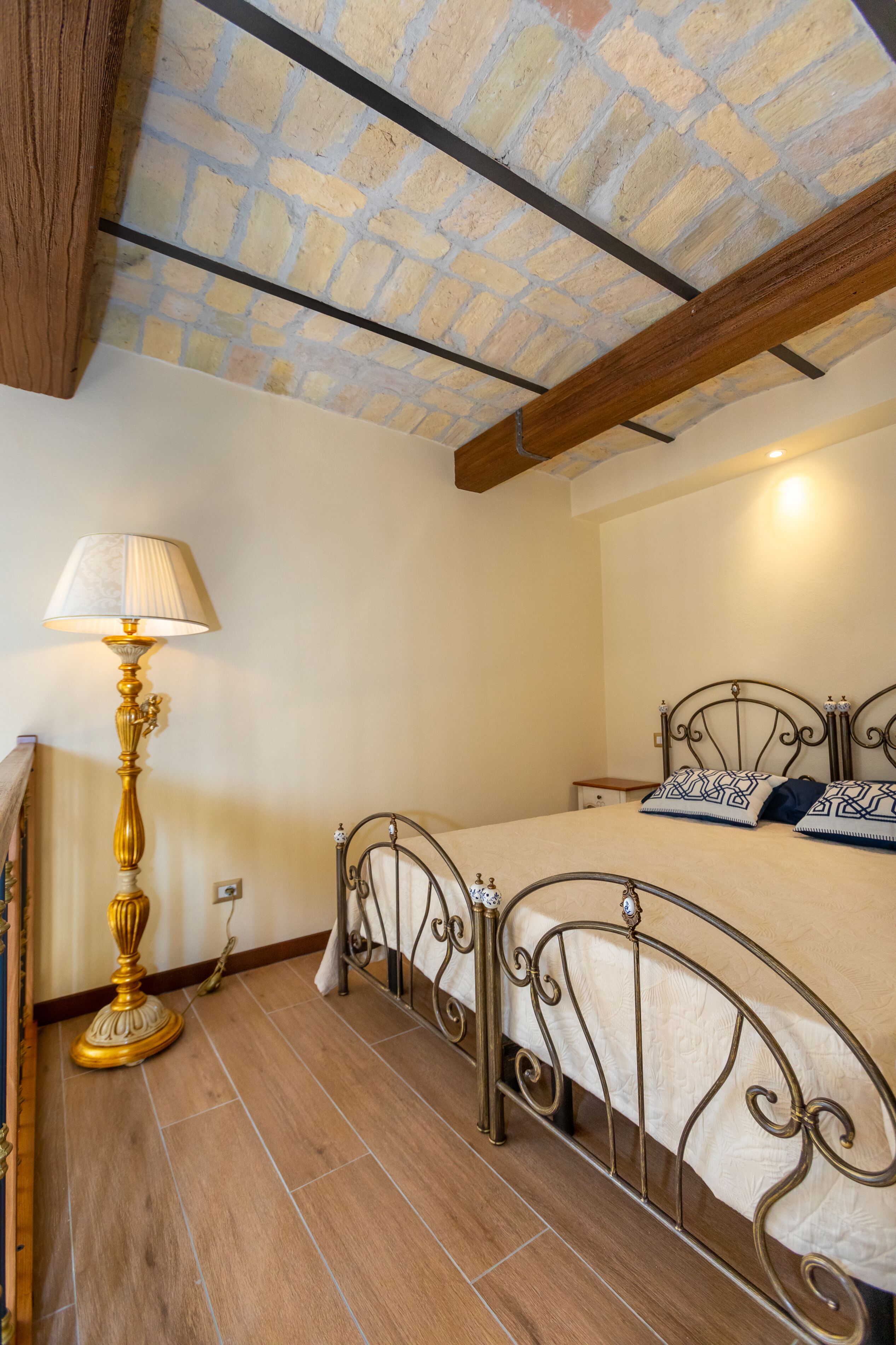 Un dormitorio con techo de madera, una cama con cabecero de metal, una lámpara de pie y una mesita de noche.
