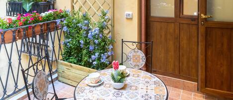 A patio with a round table and chairs, a wooden door, and a window with a white frame.