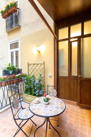 Relax in a serene outdoor space with a round table and two chairs surrounded by lush greenery and vibrant flowers.