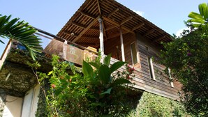 A wooden house with a thatched roof, surrounded by lush greenery and flowering plants. - Lejartre's Retreat (Mount James)