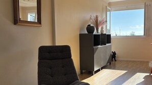 A modern living room with a dark grey armchair, a glass coffee table, and a decorative mirror on the wall.