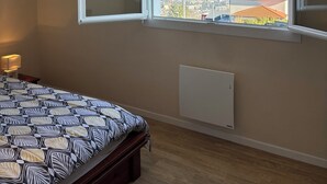 A bedroom with a bed, a radiator, a window with an open shutter, and a hanging light fixture.