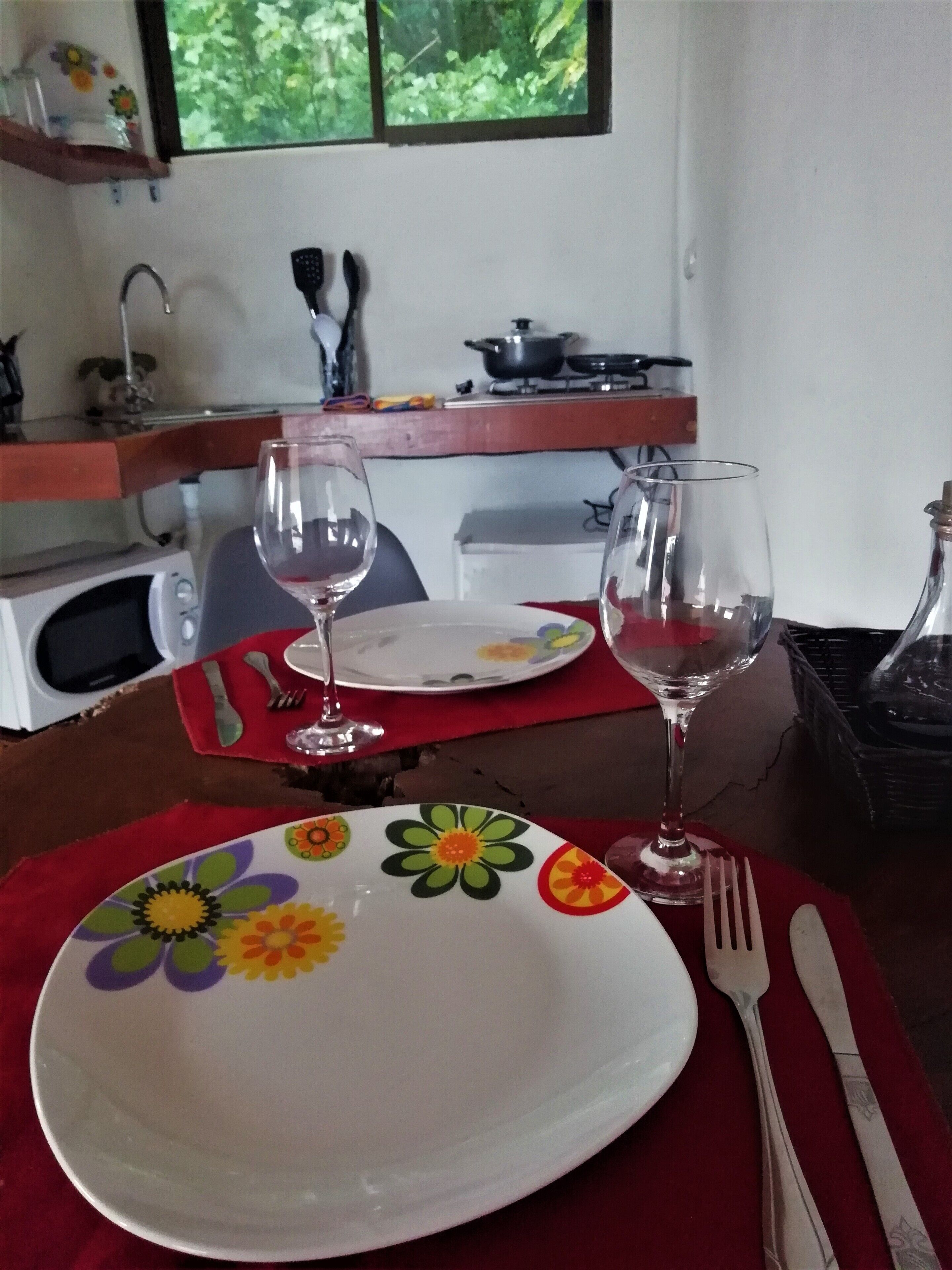 A dining table with a red placemat, a white plate with colorful floral designs, two wine glasses, and cutlery.