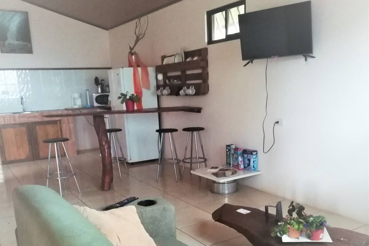 A living room with a green sofa, a wooden coffee table, and a TV mounted on the wall.