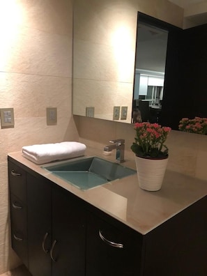 A bathroom with a glass sink, a towel on the counter, and a potted plant.