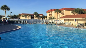 Una piscina con agua azul cristalina, rodeada de palmeras y un edificio con techo rojo.