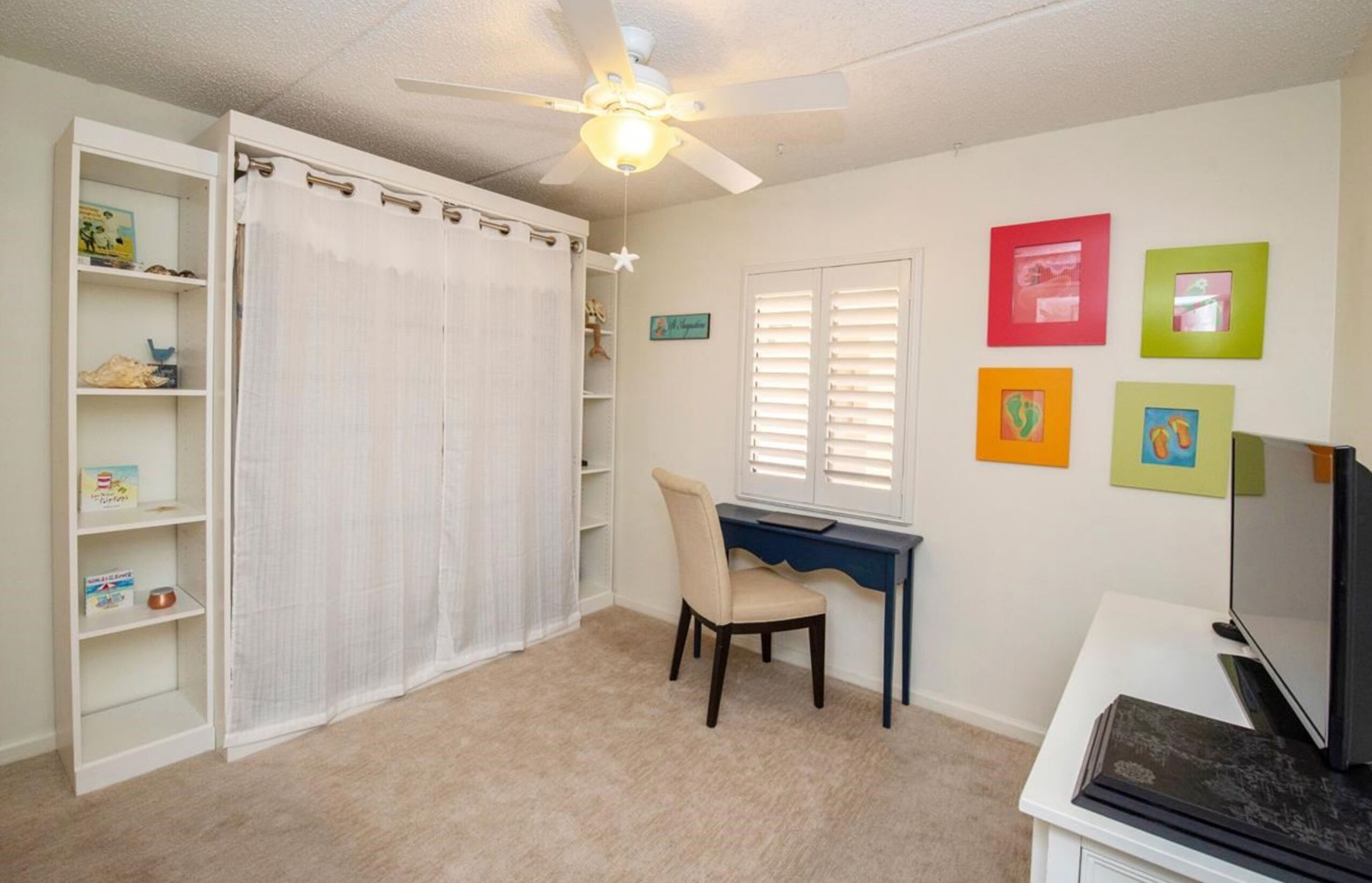 A room with a desk, chair, bookshelf, and a ceiling fan.