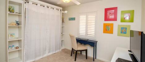 A room with a desk, chair, bookshelf, and a ceiling fan.