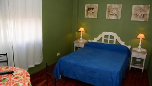 Een slaapkamer met een enkel bed, twee nachtkastjes met lampen, een stoel, en een tafel met een kleurrijke tafelkleed.