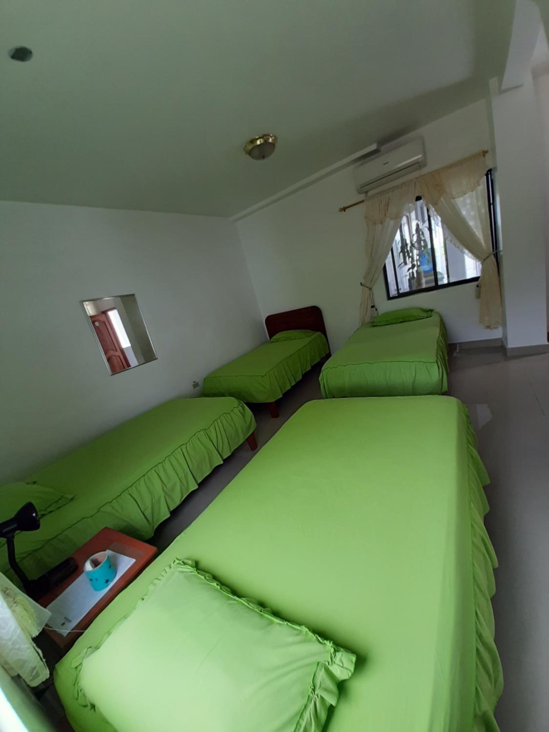 A room with three single beds, a small table with a cup, a mirror, and an air conditioning unit.