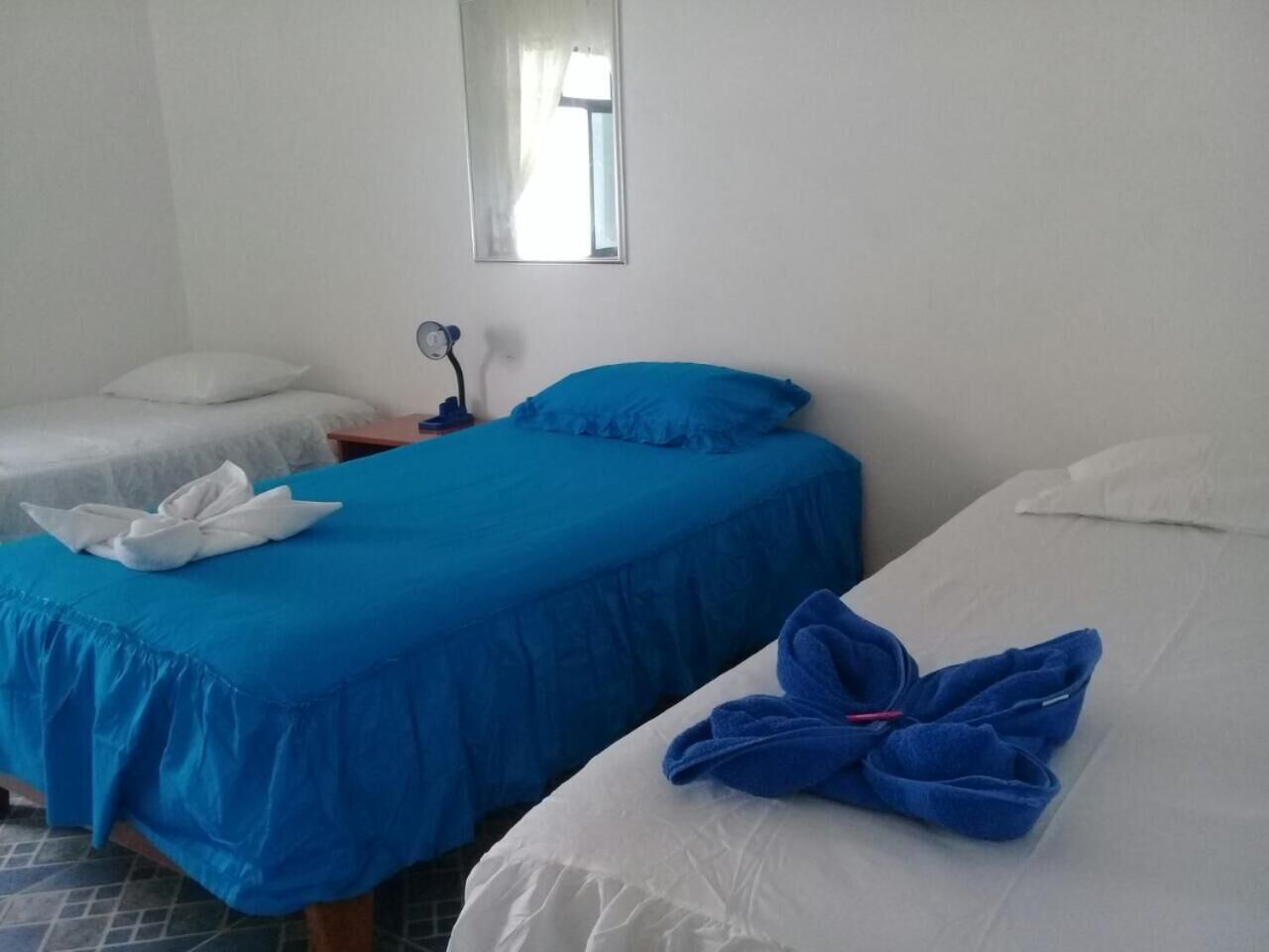 Two single beds with blue and white bedding, a small bedside table with a lamp, and a mirror on the wall.