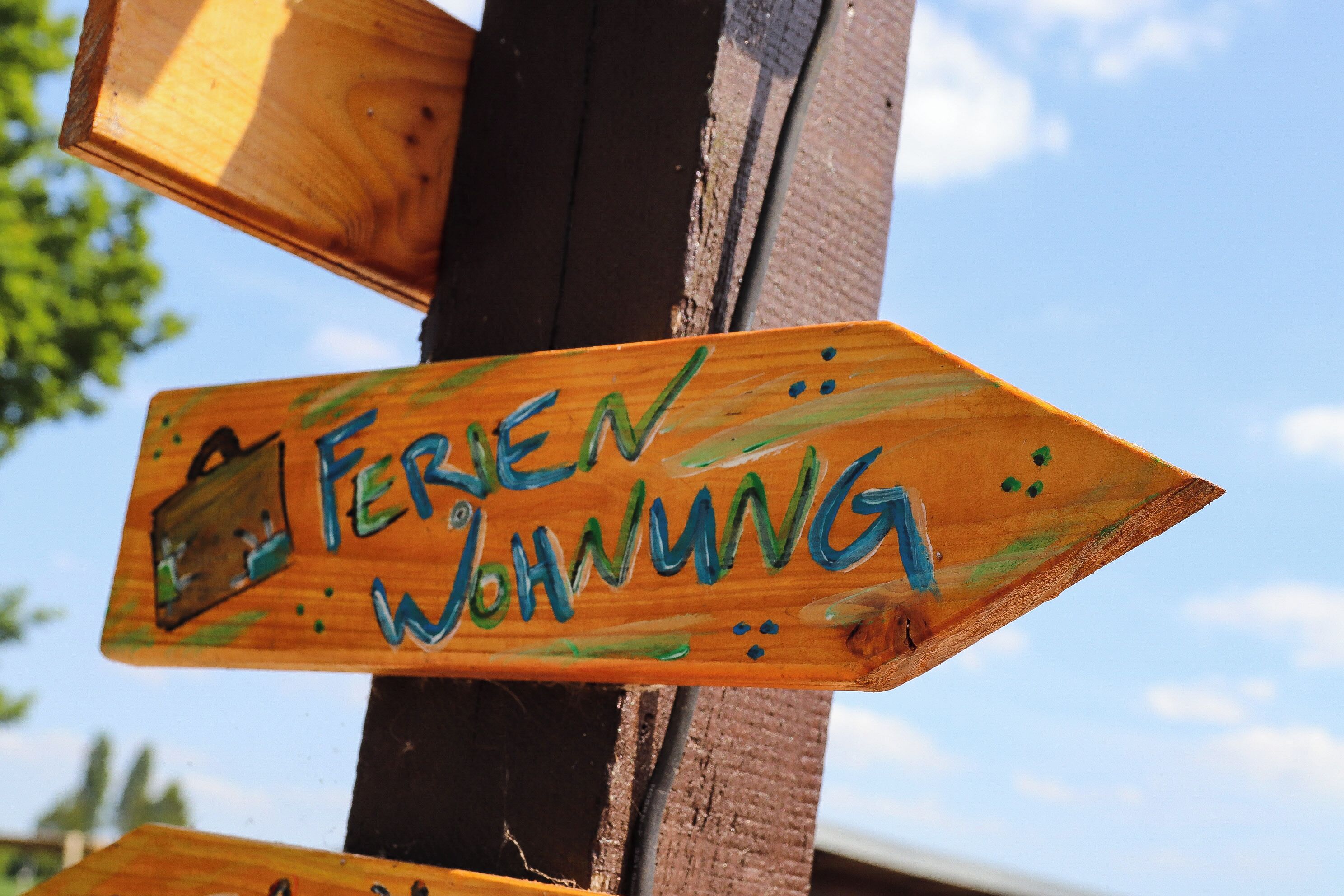 Ein hölzernes Hinweisschild mit dem Schriftzug 'FERIENWOHNUNG', das nach rechts zeigt.