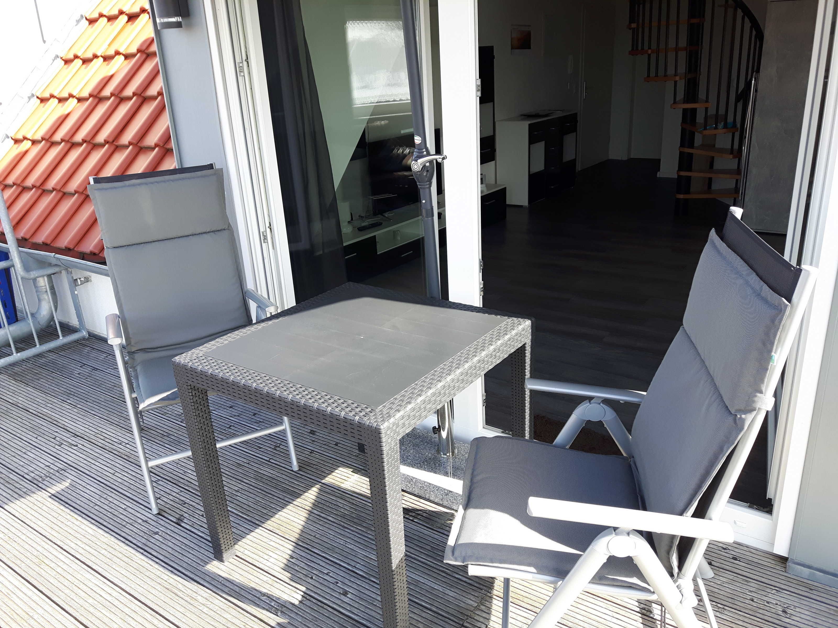 Ein Balkon mit Tisch und Stühlen, eine Glastür zum Innenbereich und eine Treppe zur Rechten.