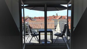 An open balcony with a table and chairs, a windmill in the background, and a view of red-roofed buildings. - Apartment Claudia (Wittmund)