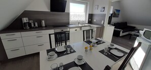 Une cuisine moderne avec un coin repas, comprenant un four encastré, une machine à café et une table à manger mise avec des assiettes, des verres et des couverts.