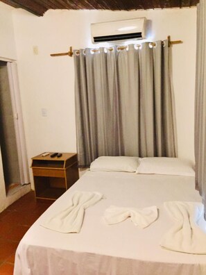 Una habitación de hotel con cama, aire acondicionado, mesita de noche y cortina.