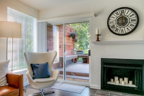 Una sala de estar moderna con chimenea, un reloj de pared grande y un portón corredizo de vidrio que da a una terraza al aire libre.