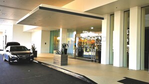 Fachada moderna de un edificio con un coche estacionado, una puerta de cristal y un carrito de objetos.