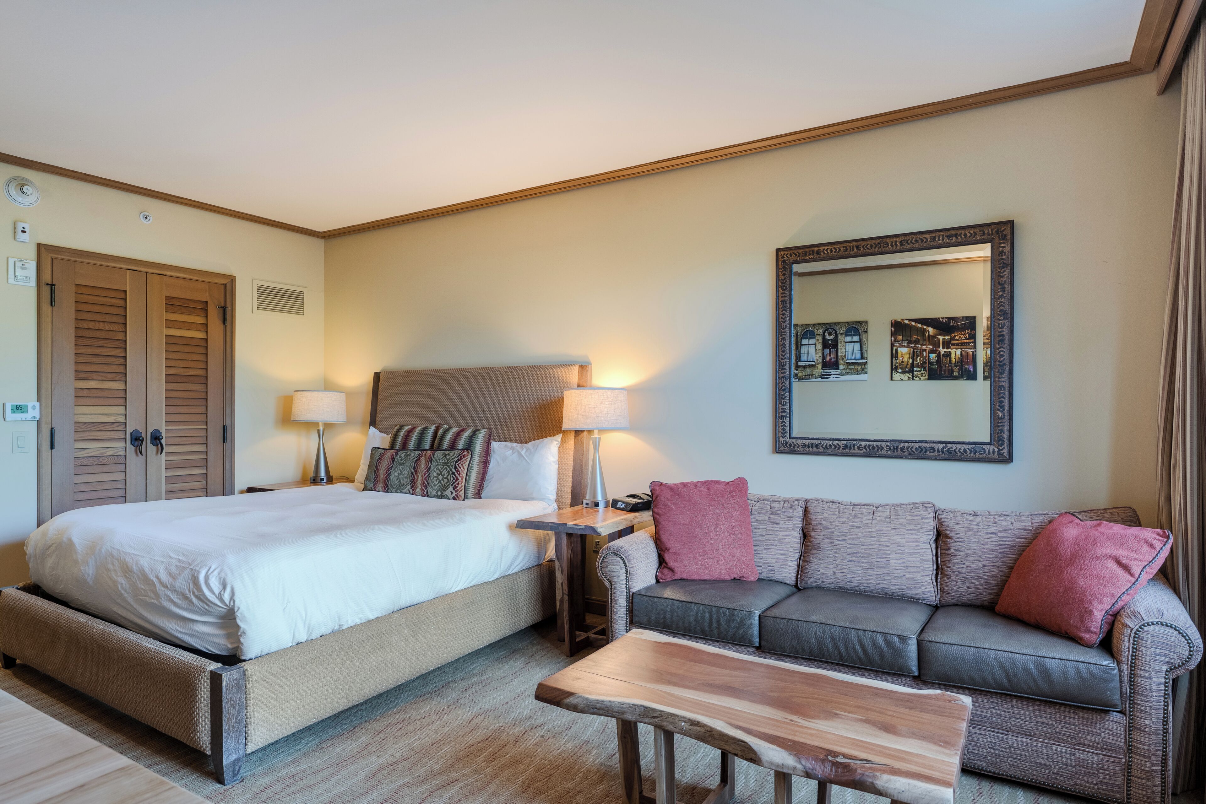 Une chambre d’hôtel avec un grand lit, un canapé, une table basse, une lampe et un miroir au mur.