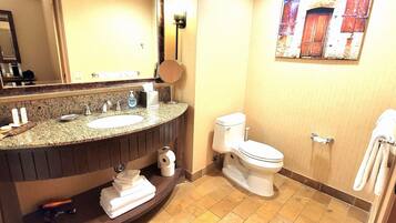 A bathroom with a granite countertop sink, a mirror, a toilet, and a towel rack.