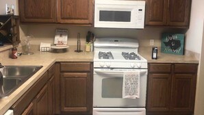 A kitchen with wooden cabinets, a white microwave, a stove, and a sign on the oven. - Cute, cozy, close duplex. (Stillwater)