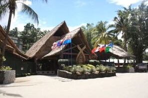 A resort with thatched-roof buildings, palm trees, and flags. - King Solomon Hotel (Honiara)