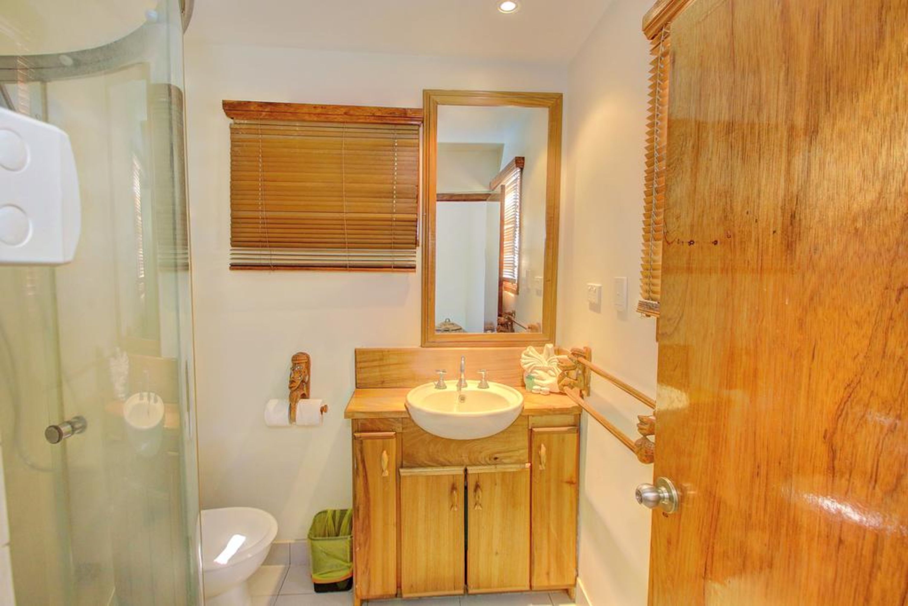 A bathroom with a wooden vanity, a sink, a mirror, and a glass shower enclosure.