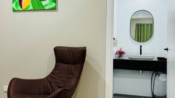 A modern bathroom with a white sink, a round mirror, and a brown chair in the corner.