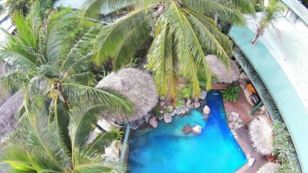 Una piscina rodeada de palmeras y sombrillas de paja, con un elemento acuático de color azul cristalino.