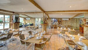Un comedor amplio con varias mesas y sillas, paredes de bambú y ventanas grandes.