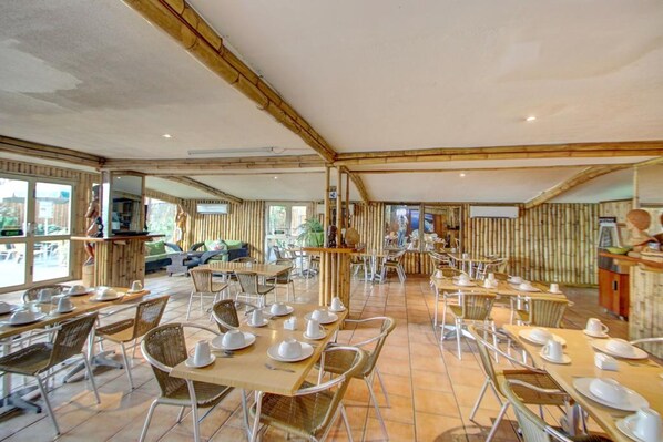 A spacious dining area with multiple tables and chairs, bamboo walls, and large windows. - King Solomon Hotel (Honiara)