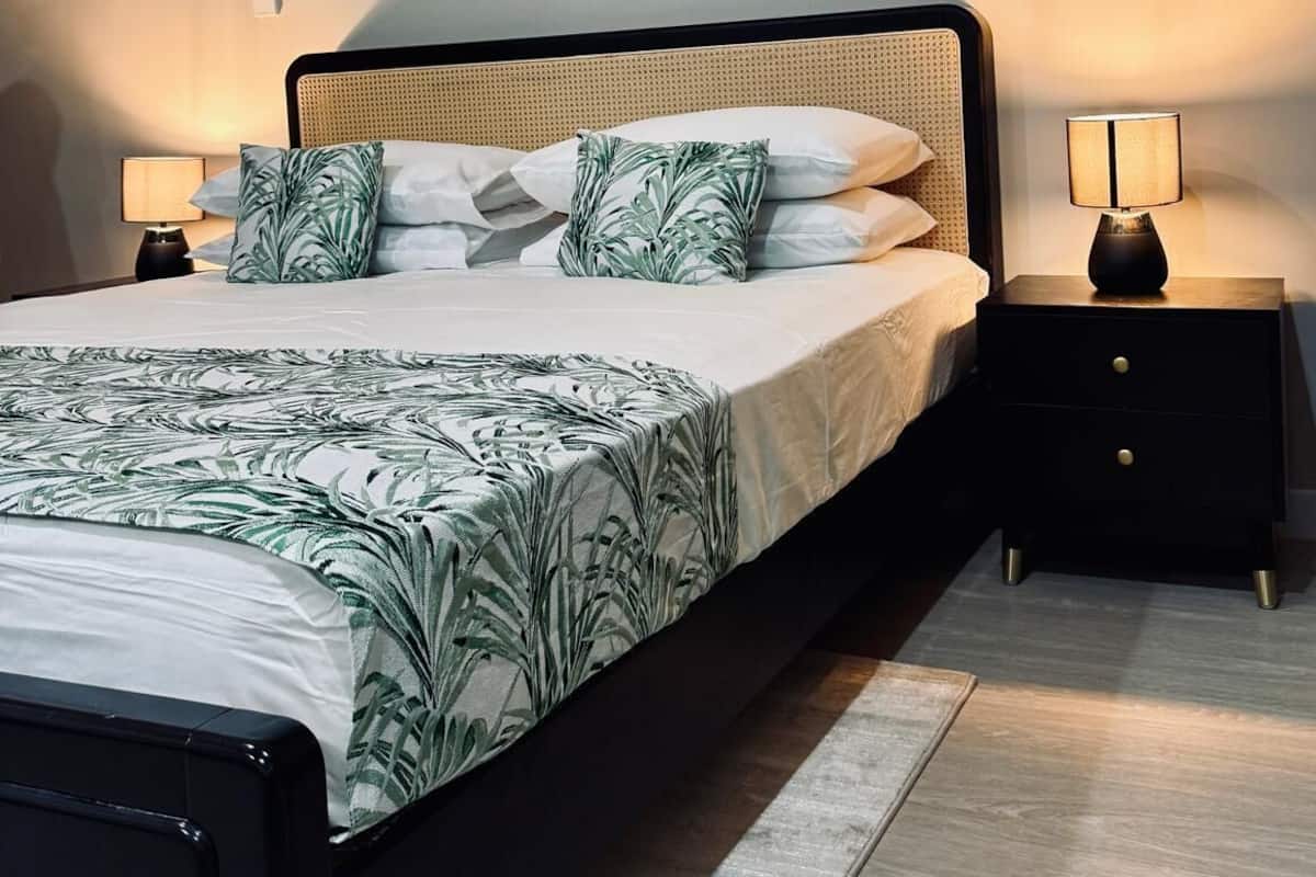 A modern bedroom with a large bed, two bedside tables, a wall-mounted artwork, and a floor lamp.