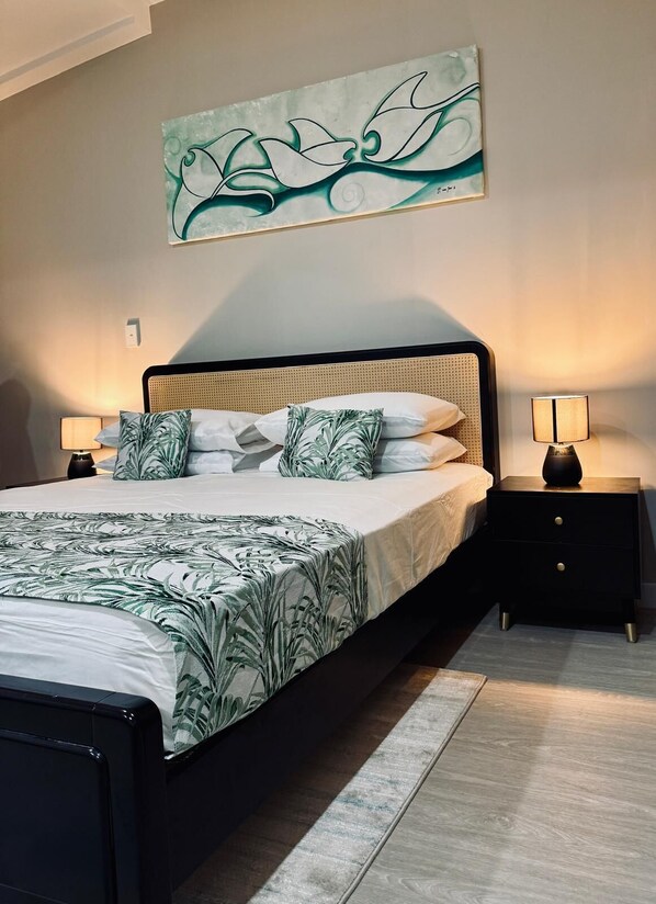 A modern bedroom with a large bed, two bedside tables, a wall-mounted artwork, and a floor lamp. - King Solomon Hotel (Honiara)
