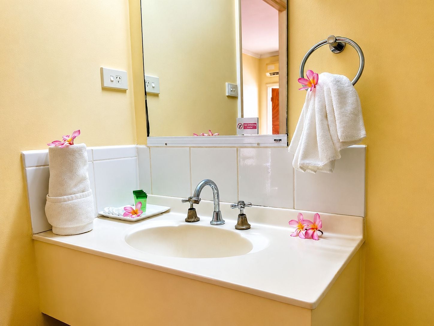 Une salle de bain avec un lavabo blanc, deux robinets, un miroir et un porte-serviettes sur lequel est posée une serviette.
