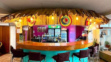 A bar area with a central counter, bar stools, and a thatched roof.