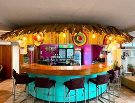 Zona de bar con mostrador central, taburetes y techo de paja.