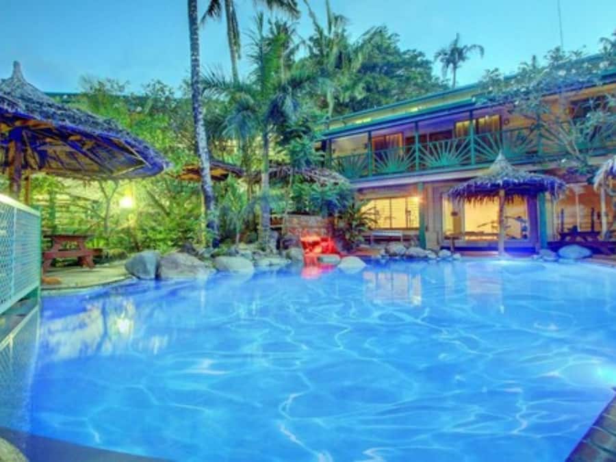 A swimming pool with a tropical setting, including palm trees and a building with a glass facade.