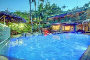 A swimming pool with a tropical setting, including palm trees and a building with a glass facade. - King Solomon Hotel (Honiara)