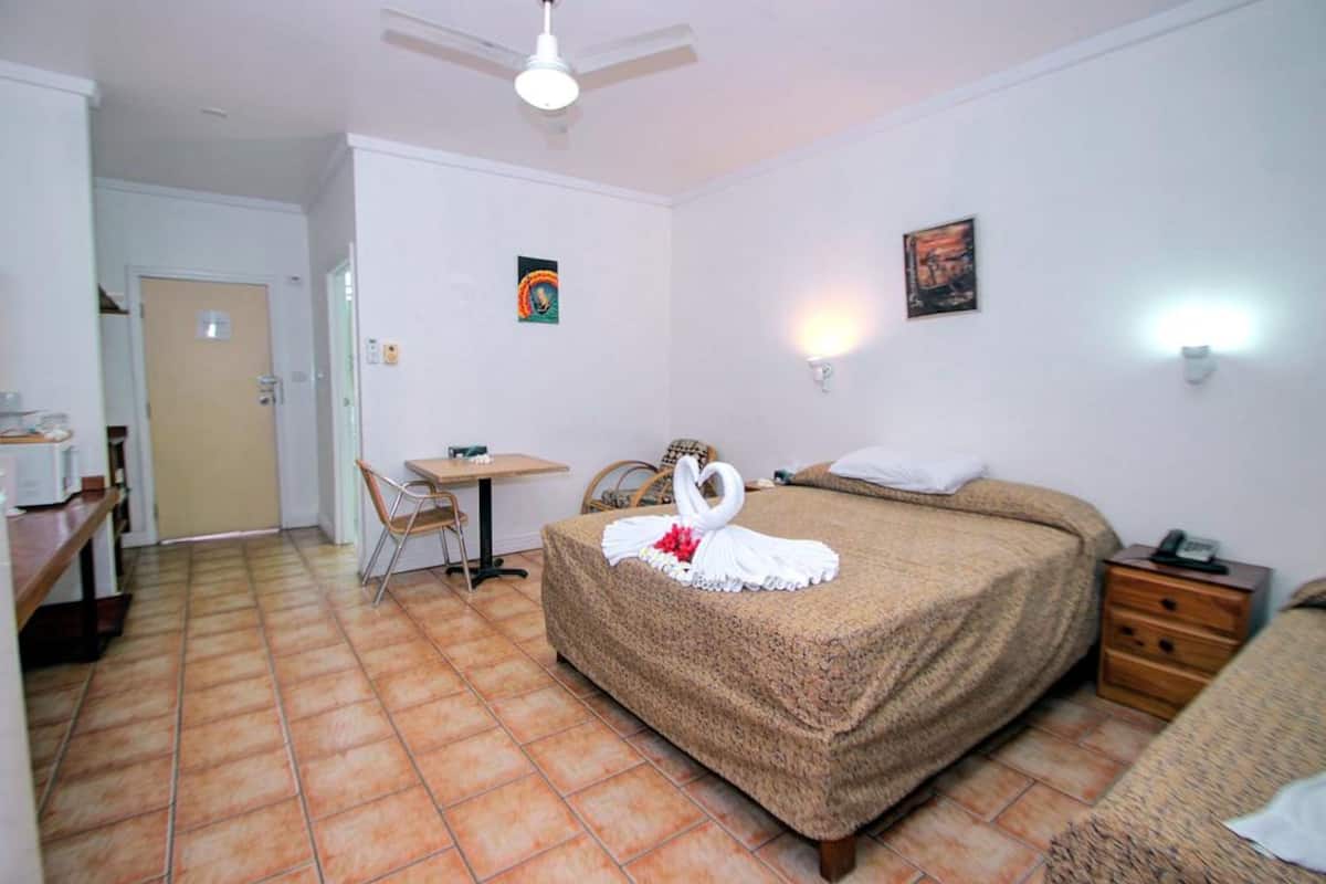 A hotel room with a bed, a desk, a chair, a nightstand, and a ceiling fan.