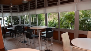 Ein Restaurant mit mehreren Tischen und Stühlen, große Fenster mit Blick auf grüne Bepflanzung.