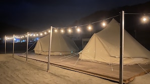 Une rangée de tentes beiges, devant lesquelles se trouve une terrasse en bois, le tout relié par des guirlandes lumineuses.