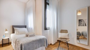 A bedroom with a bed, bedside table, lamp, chair, window, and mirror. - Sweett | Rocafort 404 (Barcelona)