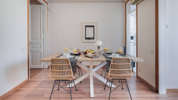 A dining area with a wooden table, two wicker chairs, and a framed picture on the wall. - Sweett | Rocafort 404 (Barcelona)
