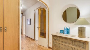 A hallway with wooden flooring, a wooden door, a mirror, a dresser with a lamp, and a framed picture on the wall. - Sweett | Rocafort 404 (Barcelona)