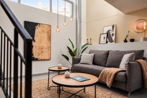 Un salon moderne avec un canapé gris, deux petites tables rondes et un grand tableau abstrait.