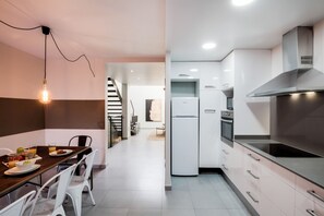 Une cuisine moderne avec des meubles blancs, une hotte en acier inoxydable et un réfrigérateur.