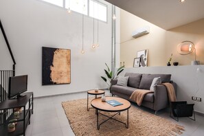 Un salon moderne avec un canapé gris, une table basse, un téléviseur posé sur un meuble et un grand tableau abstrait accroché au mur.