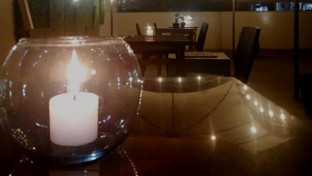 A dining area with a table under a tent-like structure, a candle in a glass bowl, and string lights. - Hotel Brickell (Lima)