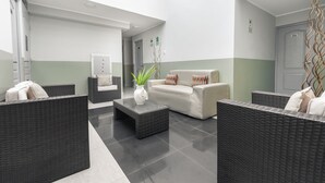 A modern lobby with wicker furniture, a white sofa, a coffee table, and a reception area. - Hotel Brickell (Lima)